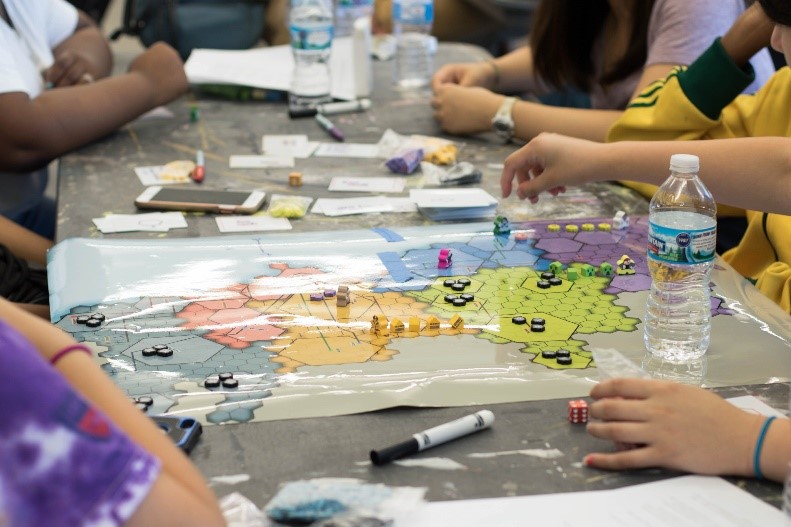 High school students seated at a table with a glossy, laminate test model of the Hexacago game and game pieces on top of it