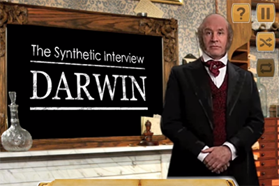 Still shot of a virtual Charles Darwin standing by a chalkboard that reads The Synthetic Review: Darwin and waiting for the app user to make their selection.