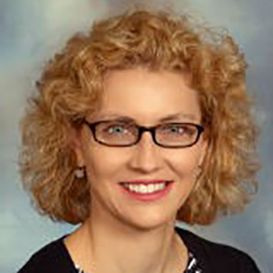 Profile picture of Carrie Sims with strawberry blonde curly hair and eyeglasses, smiling.