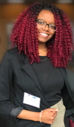 Photo of Charmaine Nganje, with curly red shoulder-length hair and eyeglasses, smiling..