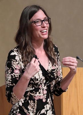 Melissa Wilson wearing a floral dress and speaking beside a podium during her lecture.