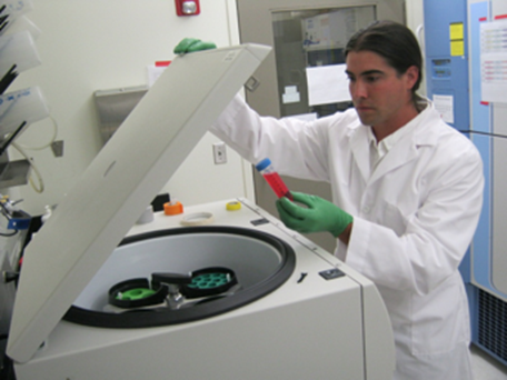 Joshua Marceau examining a specimen in front of a large centrifuge.