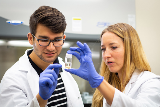 Nance holding a test tube and showing it to another researcher in her lab.