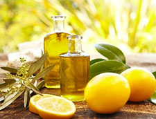 Whole and sliced lemons, two jars of lemon oil, and lemon leaves on a wooden table.