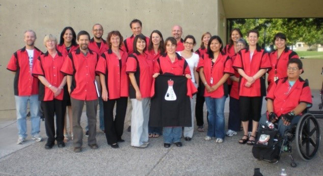 A group of 19 people outside posing for a picture in matching red shirts