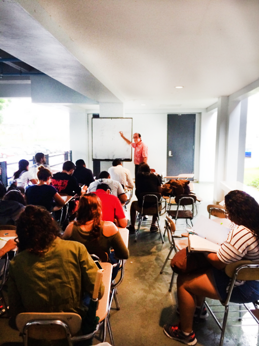 Dr. Tremblay standing at a whiteboard and teaching students who are sitting at desks in a hallway.