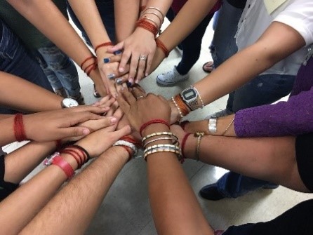 A group of students standing in a circle with their hands extended toward the center.