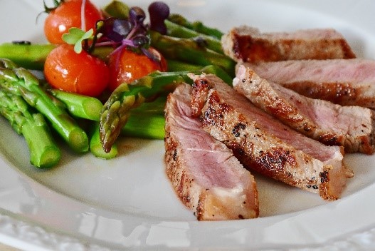 A plate with sliced meat, asparagus, and tomatoes.