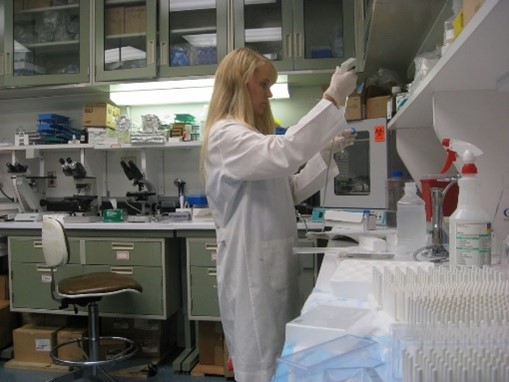 Dr. Bohannon working in a lab while wearing a lab coat and gloves.