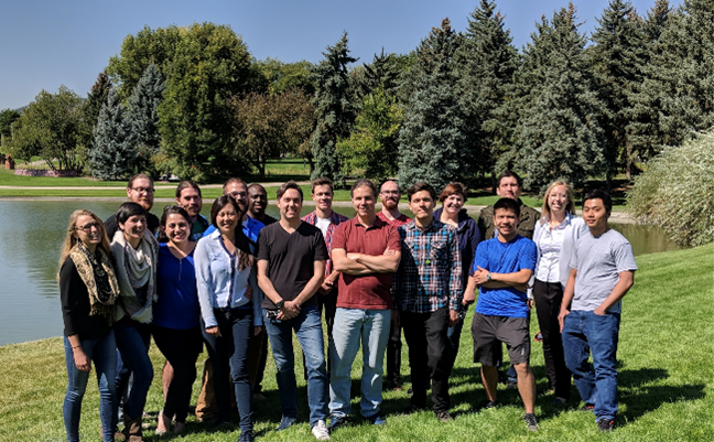 A group of people standing outside in front of a pond.