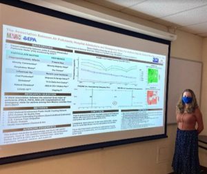 Raven standing next to a projector screen showing a research poster.