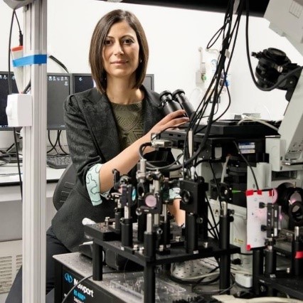 Dr. Lakadamyali sitting behind a large, complex microscope in a lab.