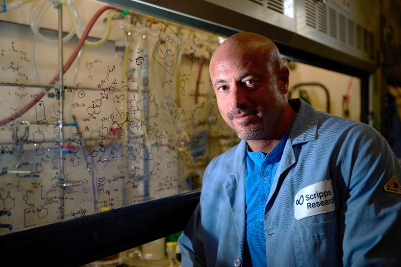 Dr. Baran standing in front of a chemistry fume hood with molecular structures drawn on it.