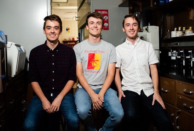 From left to right: Caleb, Paul, and Adam Worsley sitting on stools in a chemistry lab.