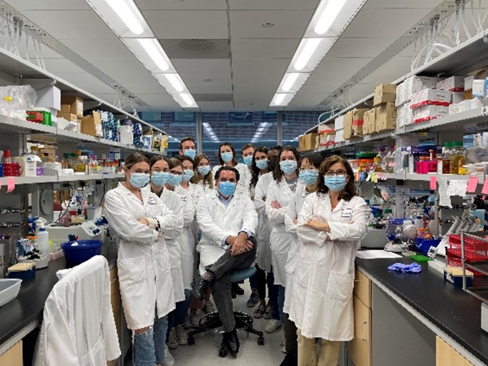 A group of 13 researchers standing in a lab, with Dr. Torres (seated center), all wearing lab coats and surgical masks.
