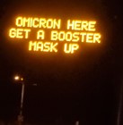 A digital road sign with the text, “Omicron here. Get a booster. Mask up.”