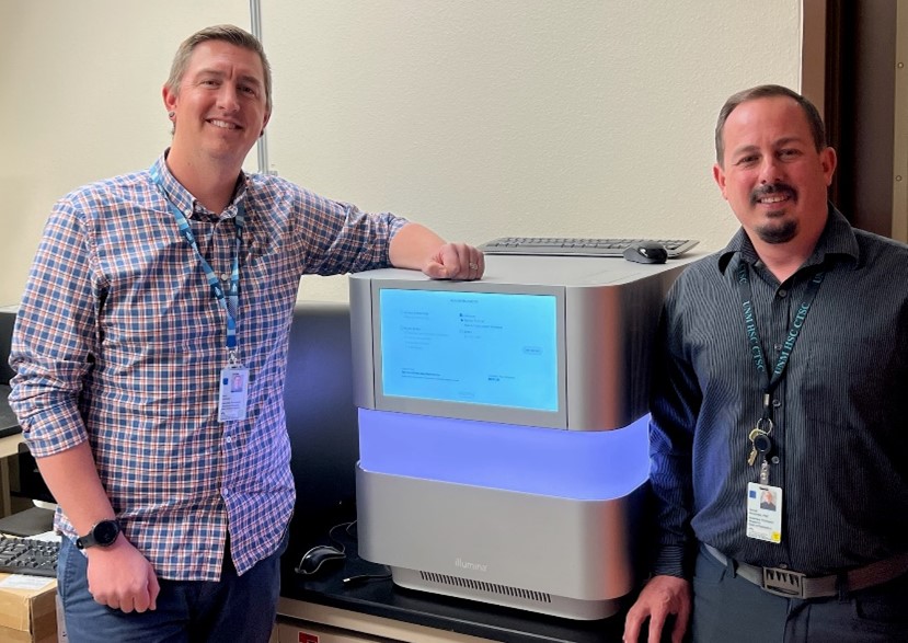 Drs. Domman and Dinwiddie standing on either side of a large cube-shaped device with a digital screen on a table.