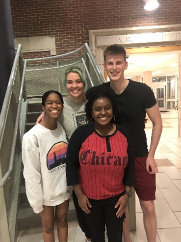 Four students standing in front of a campus building staircase.