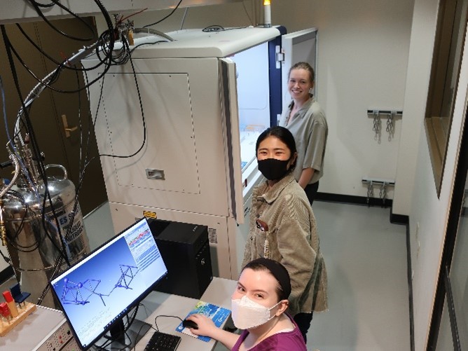 Three researchers in a room with a computer and a large refrigerator-like piece of equipment connected to a liquid nitrogen tank.