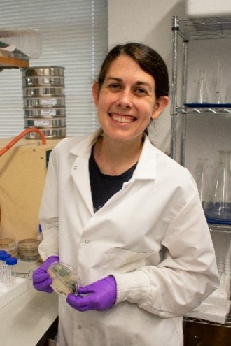 Dr. Parkinson wearing a lab coat and gloves and holding a Petri dish.