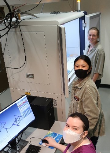 Three researchers in a room with a computer and a large refrigerator-like piece of equipment connected to a liquid nitrogen tank.
