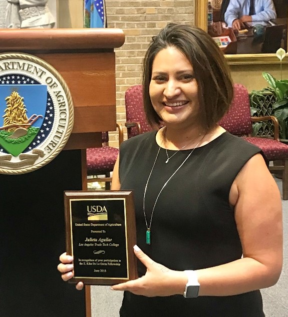 Dr. Julieta Aguilar posing with a plaque in front of a podium with the USDA seal on the front.