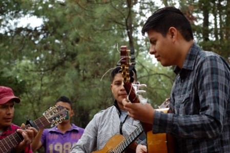 Dr. Márquez-Zacarías and two other people playing guitars outdoors, with another person standing in the background.