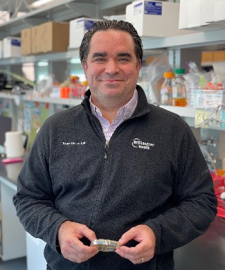 Dr. Torres standing in a lab holding a Petri dish.