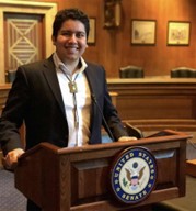 Alec J. Calac standing behind a podium with the Great Seal of the United States surrounded by the words “United States Senate.”