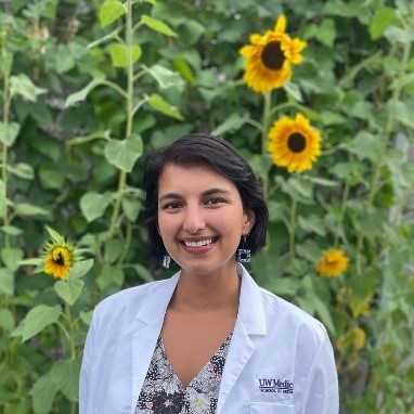 Amelia Wilhelm wearing a white doctor’s coat and posing outside in front of sunflowers.