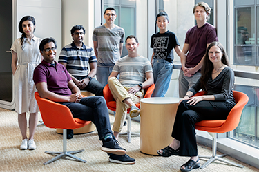 Drs. Carpenter and Singh with six lab members by tall glass windows inside a building.