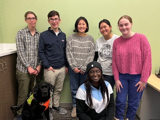 Five people standing behind one dog and one person kneeling in front.