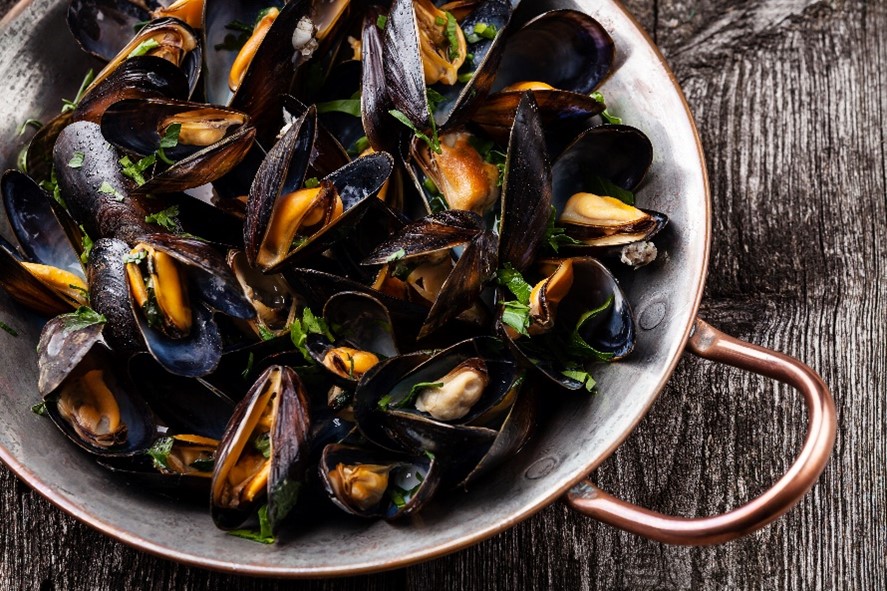 Cooked mussels sprinkled with green herbs in a pot.