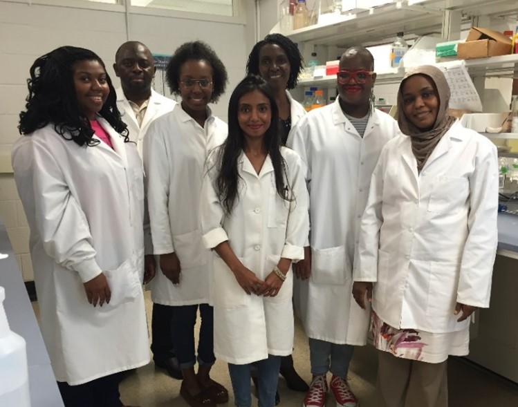 Dr. Ongeri and six others, all wearing lab coats and posing for a group picture in the laboratory.