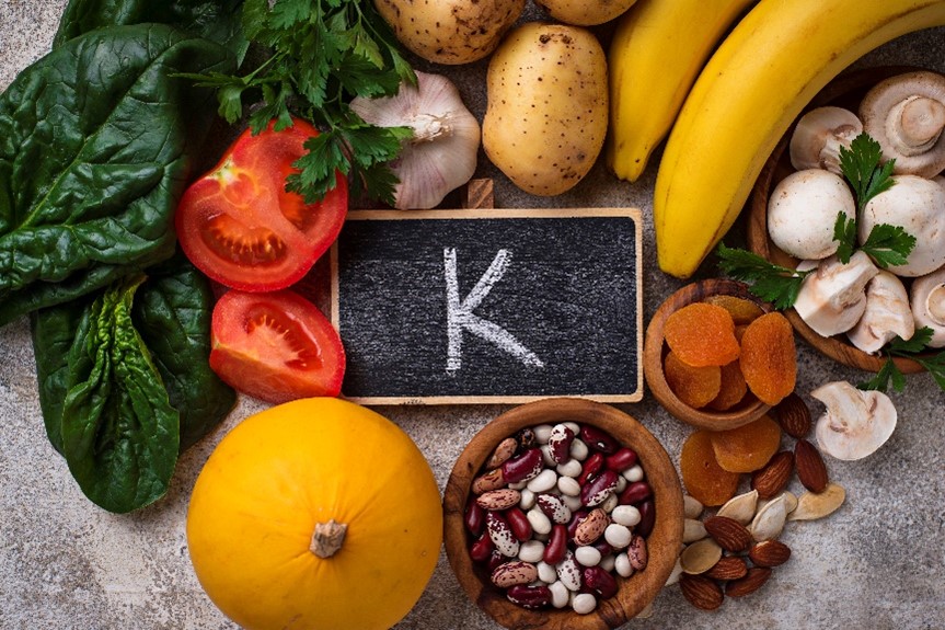 A variety of foods surrounding a small chalkboard with potassium’s symbol “K” written on it.