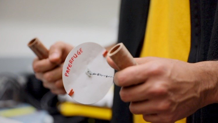 A person holding tubes in each hand connected by strings with a piece of paper in the middle. 