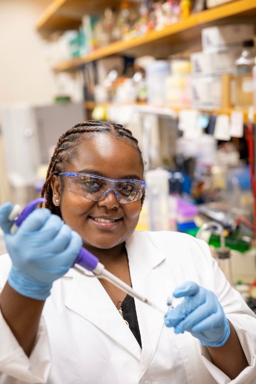 A smiling Hasset working with a pipette and a small tube in the laboratory.