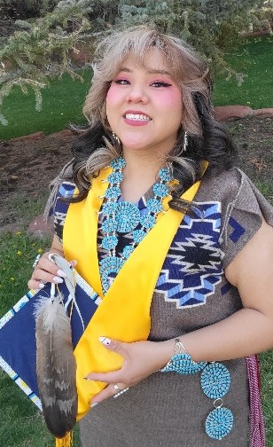 Chantel wearing a traditional Native American dress and holding a graduation cap.