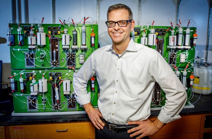 A portrait shot of Dr. Martin Burke standing in front of complex machinery.