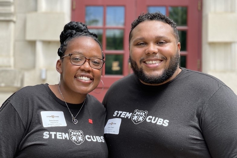 Dr. Gilyot smiling for a photograph with another mentor. They're wearing matching shirts with the STEM Cubs logo.