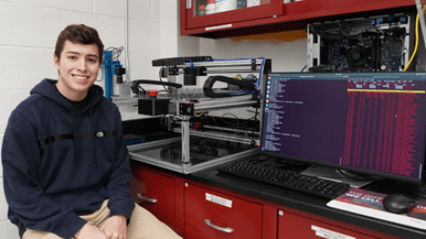 Colton Pelletier posing in front of complex laboratory machinery and a computer screen.