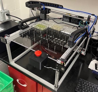 Complex machinery with four dishes containing a yellow liquid. 