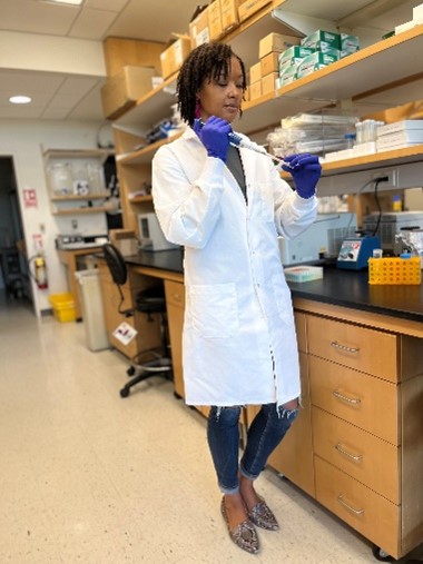 Dr. Spriggs in the lab wearing a lab coat and gloves and using a pipette.